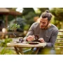 Homme assemblant le bonsaï LEGO sur une table de jardin, avec l'arbre miniature aux feuilles vertes visible à côté Homme assemblant le bonsaï LEGO sur une table de jardin, avec l'arbre miniature aux feuilles vertes visible à côté