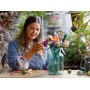 Femme assemblant le bouquet LEGO avec des fleurs colorées dans un vase en verre turquoise sur une table en bois