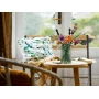 Bouquet LEGO coloré dans un vase vert sur une table en bois près d'une fenêtre avec coussin fleuri