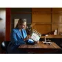 Femme en blazer bleu tenant une radio LEGO rétro blanche et orange dans un salon moderne avec bibliothèque en bois Femme en blazer bleu tenant une radio LEGO rétro blanche et orange dans un salon moderne avec bibliothèque en bois