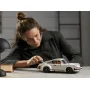 Femme assemblant la Porsche 911 LEGO blanche sur un bureau, se penchant pour ajuster les détails du modèle Femme assemblant la Porsche 911 LEGO blanche sur un bureau, se penchant pour ajuster les détails du modèle